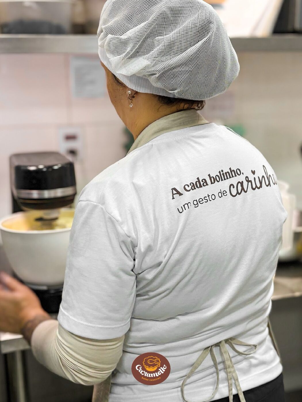 Confeiteira de costas com o uniforme da Caramello preparando uma massa